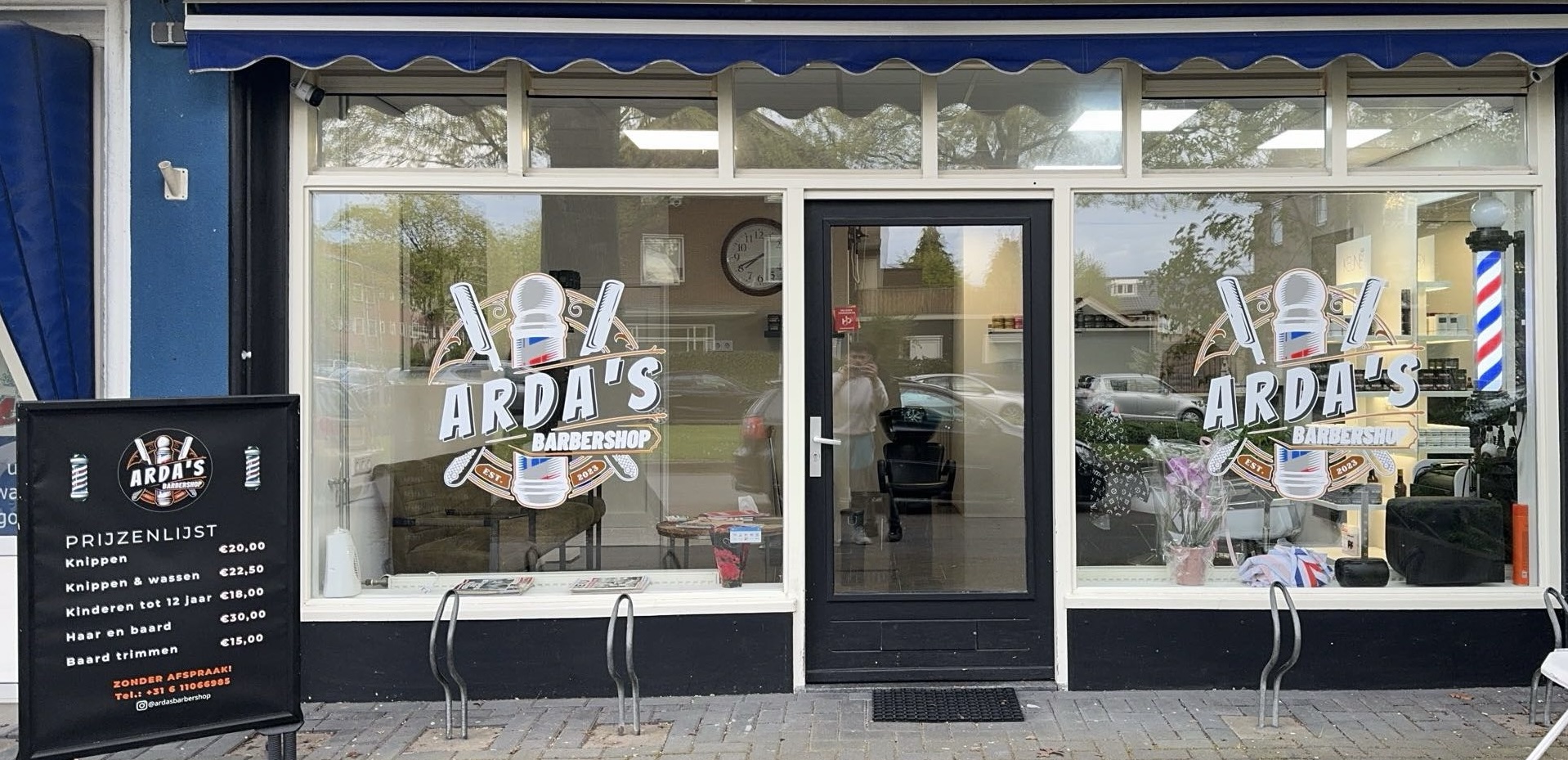 Gevel van Arda's Barbershop met de raambelettering, barberpaal en het prijzenbord