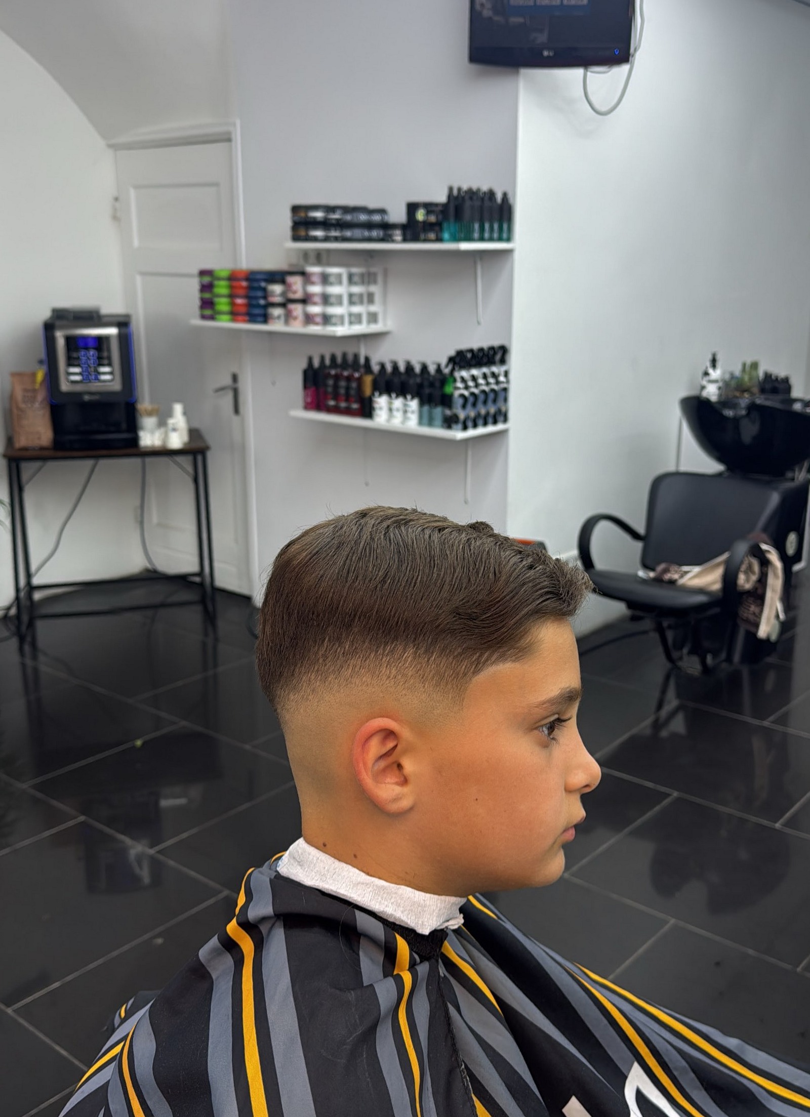 Jongen met een strakke fade en zijscheiding, zijaanzicht in de zaak